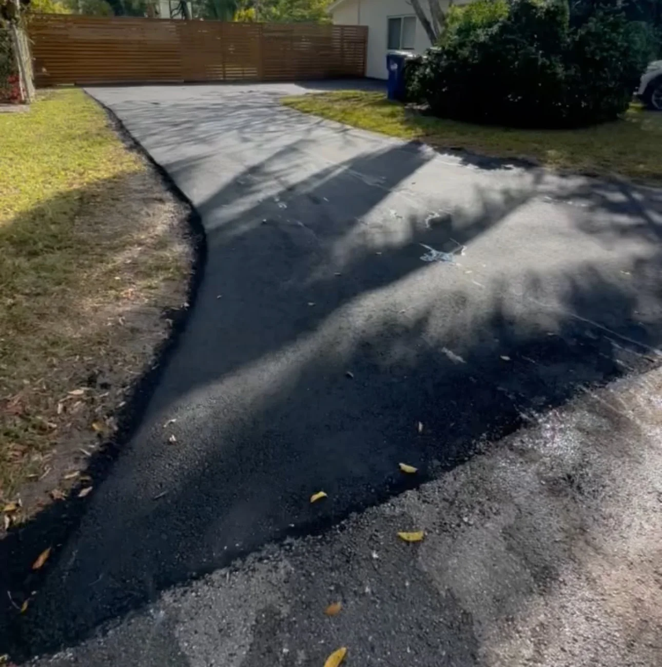 Fresh black asphalt driveway curving to a wood fence gate, Miami, FL