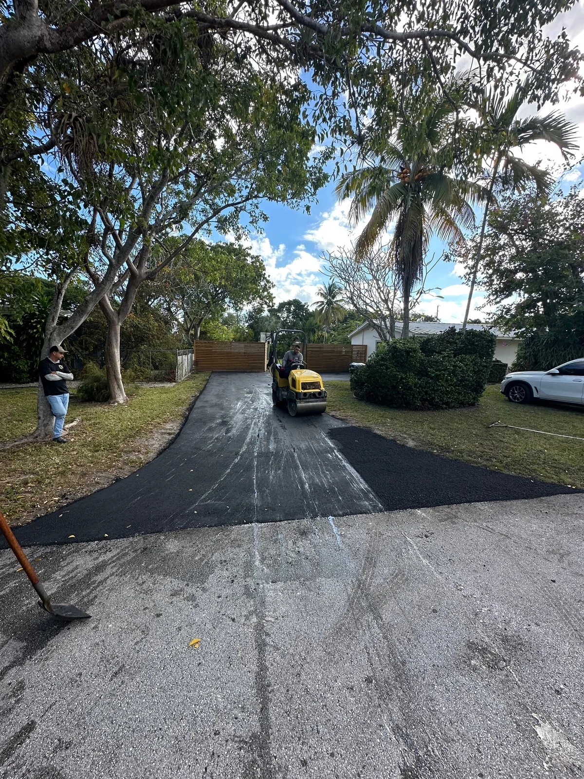 Roller compacting fresh asphalt on a residential driveway under trees, Miami, FL