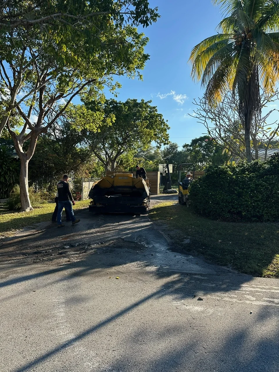 Asphalt paving machine backed onto a residential driveway with the crew, Miami, FL