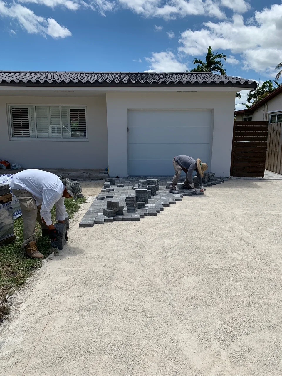 Two crew members laying charcoal pavers at the garage end of a driveway, Miami, FL