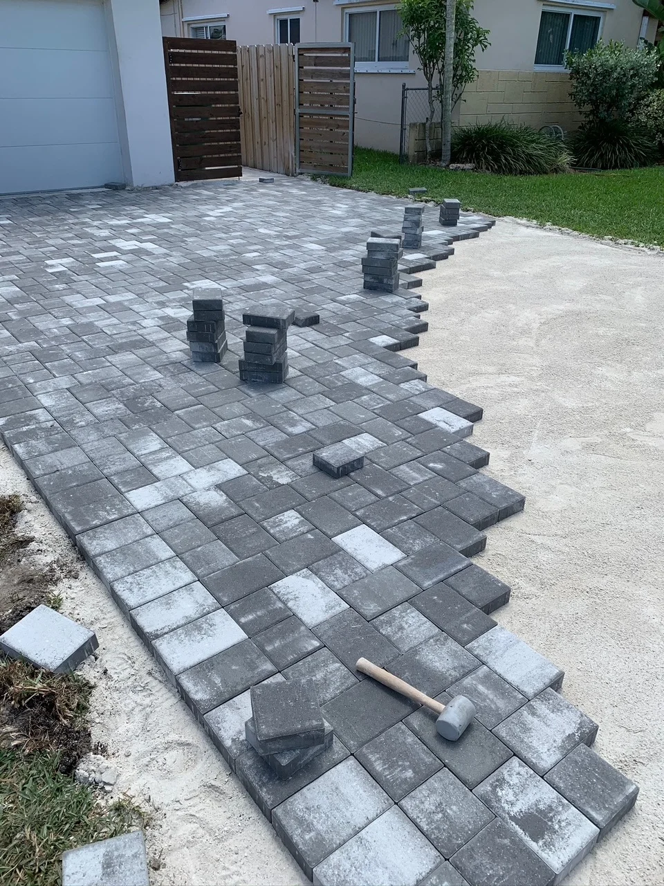 Charcoal pavers being set with a rubber mallet on a bedding-sand driveway, Miami, FL