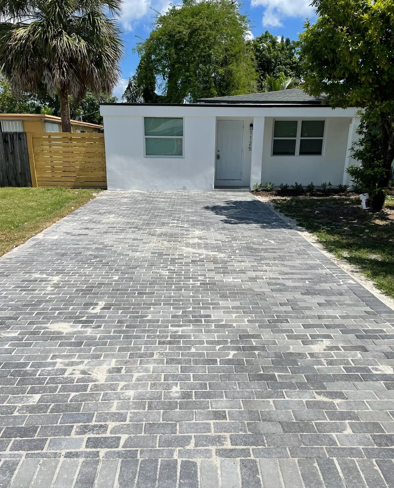 Charcoal paver driveway in front of a small white house with a wood fence, Miami, FL