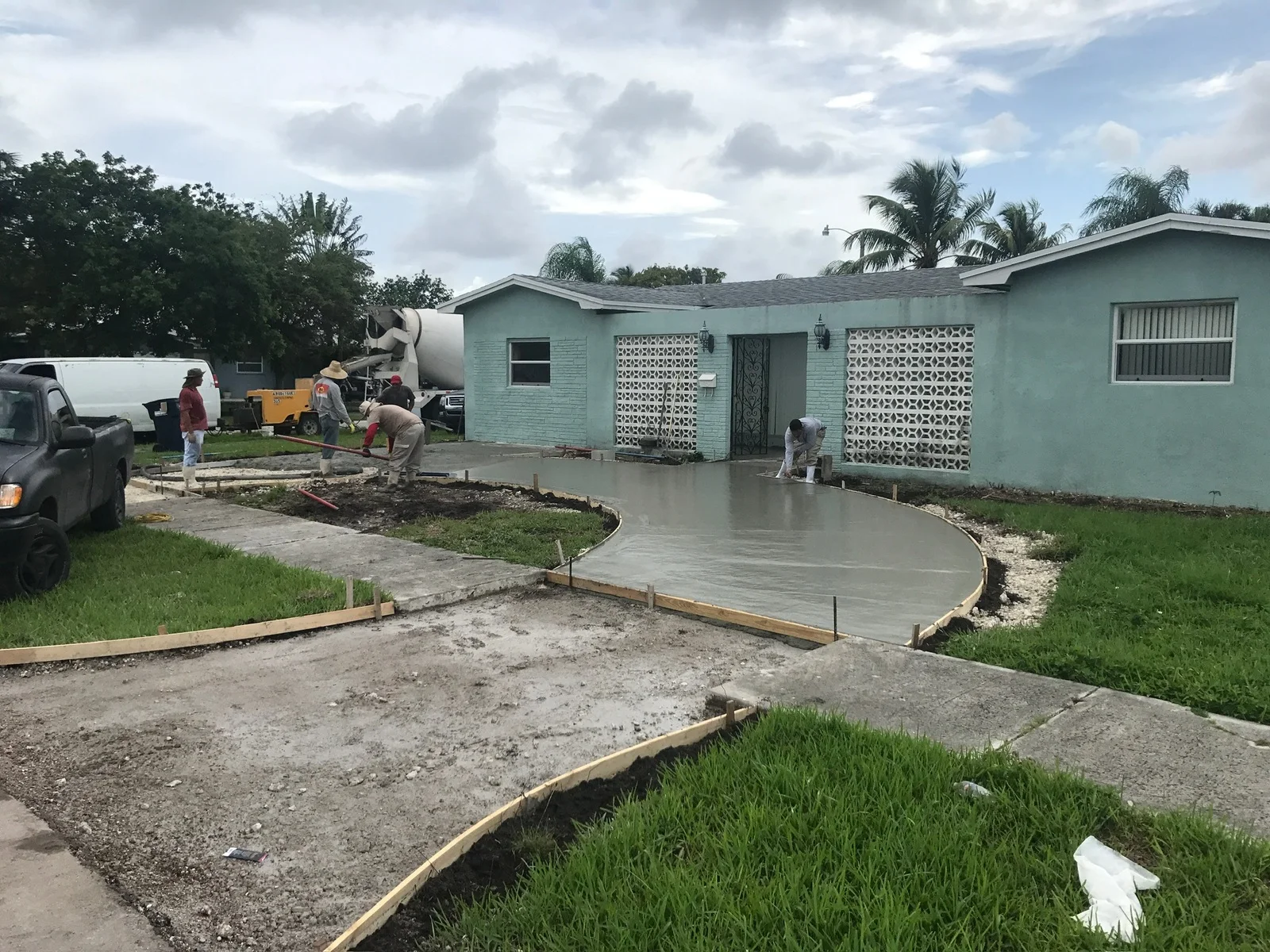 Crew pouring and screeding a new concrete driveway in front of a small turquoise house, Miami, FL