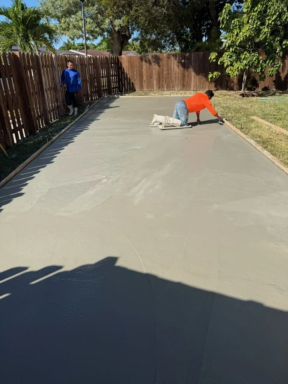 Crew finishing a fresh concrete pad along the side of a house, Miami, FL