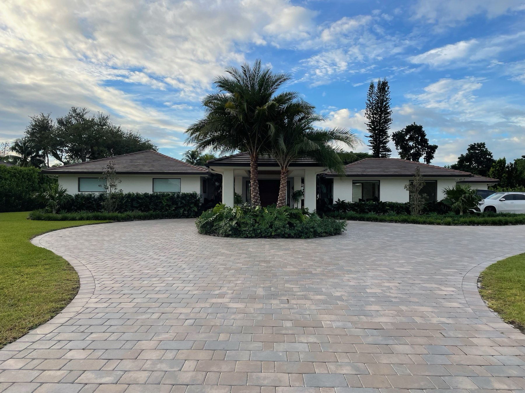 Circular paver driveway curving around twin palms at a white single-story Florida home