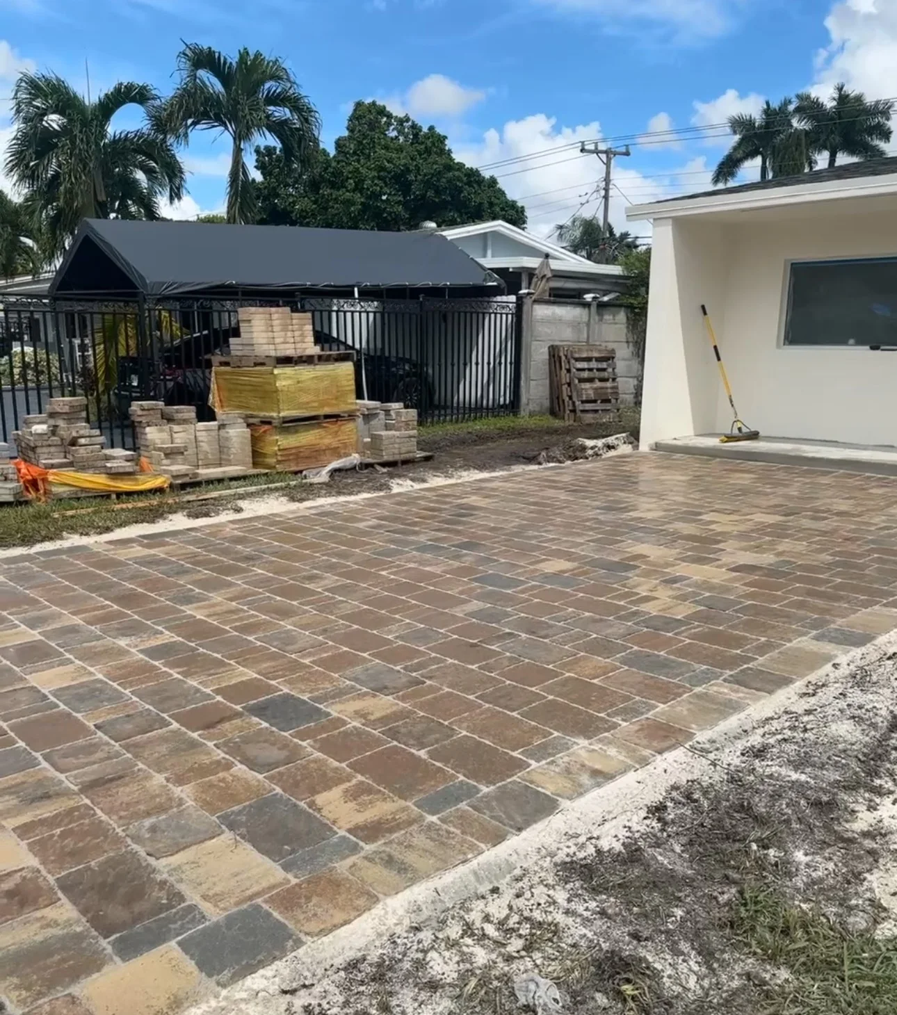 Multicolor pavers laid across a driveway with pallets staged by the carport, Miami, FL