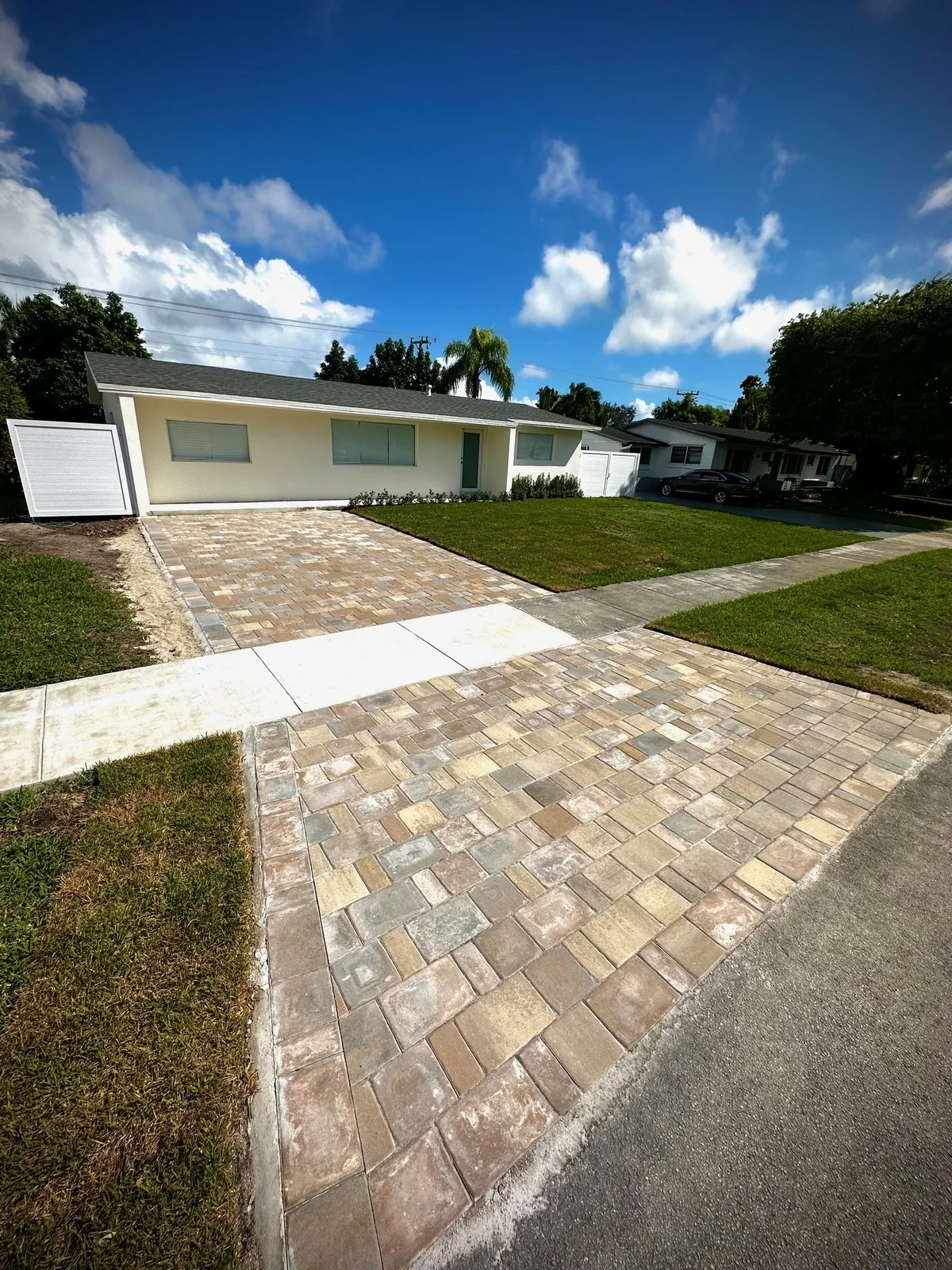 New paver driveway and street apron under a deep blue sky at a pale yellow house, Miami, FL