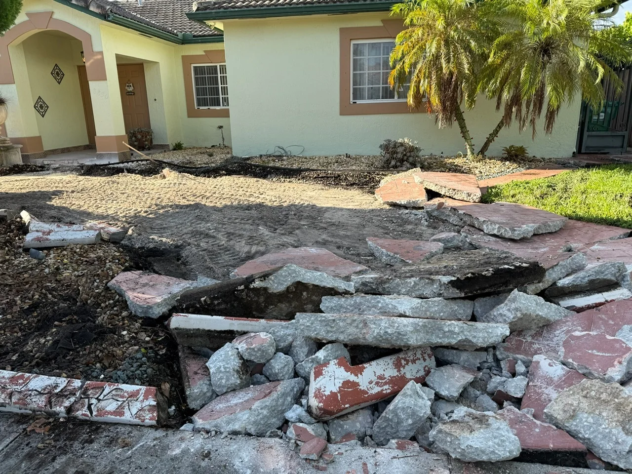 Old pavers broken out and piled in front of a house before a new travertine driveway, Miami, FL