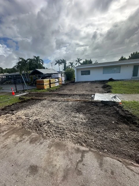 Driveway excavated to depth with pallets of pavers ready at the fence, Miami, FL