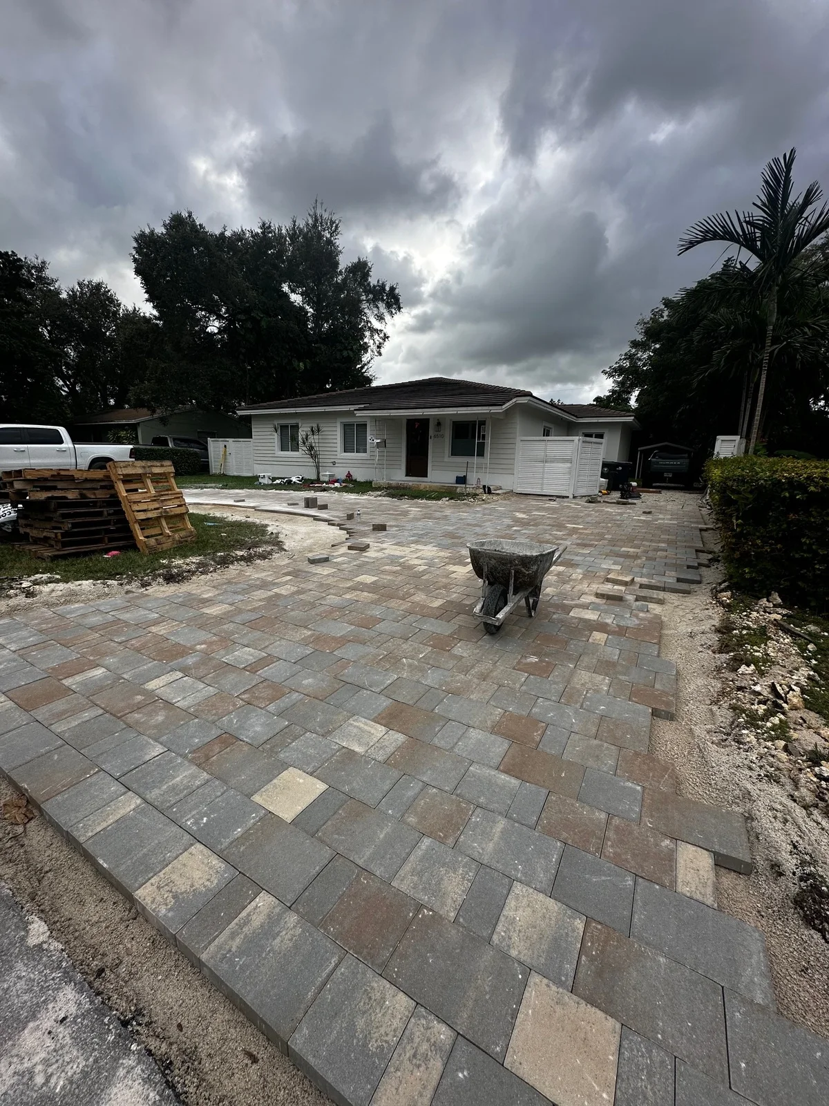 Pavers going down on a driveway with pallets staged under a stormy sky, Miami, FL