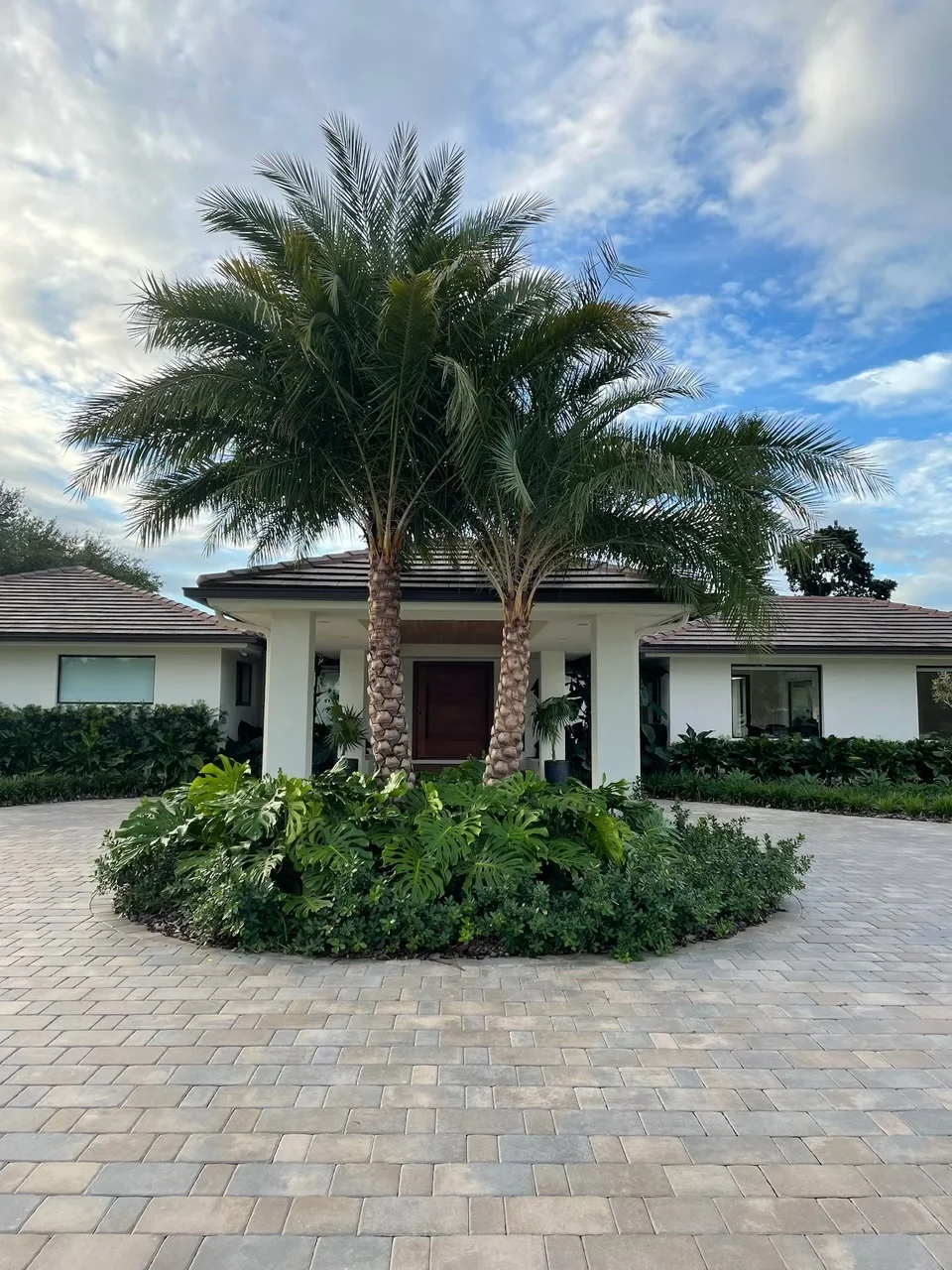 Paver motor court circling a planted island with twin palms at a white house, Miami, FL