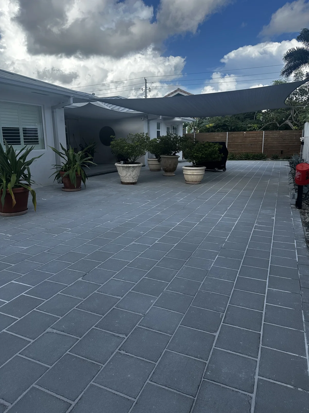 Grey paver patio under a shade sail between a house and a privacy wall, Miami, FL
