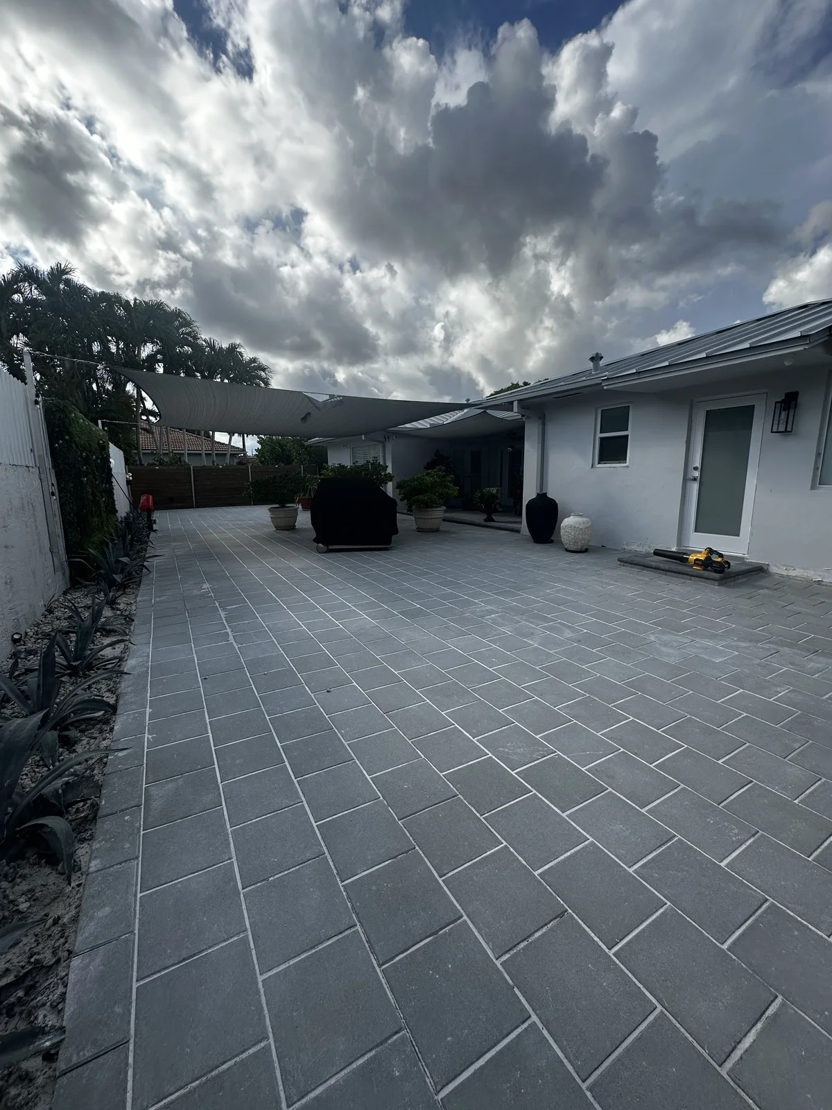 Paver patio floor running to a privacy wall beneath a shade sail, Miami, FL