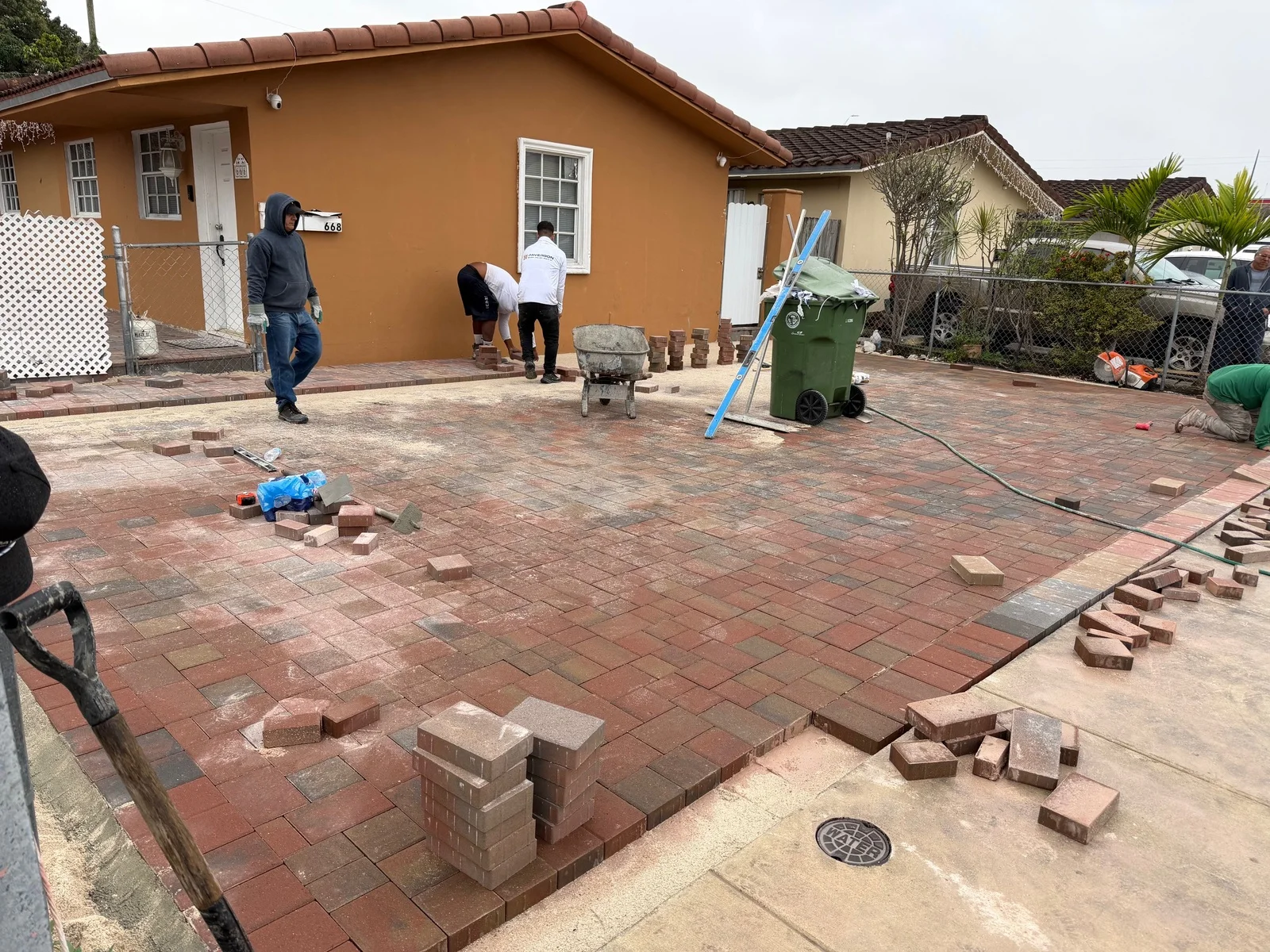 Red-blend paver driveway being laid in front of an orange house, Miami, FL