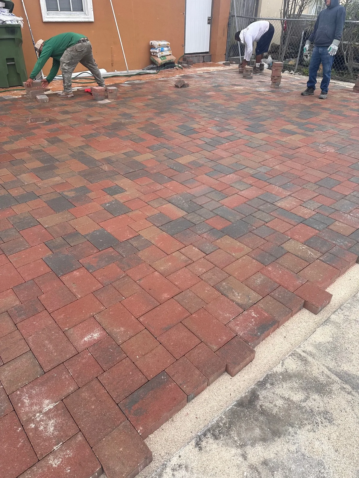 Crew laying red-blend pavers across a front drive, Miami, FL