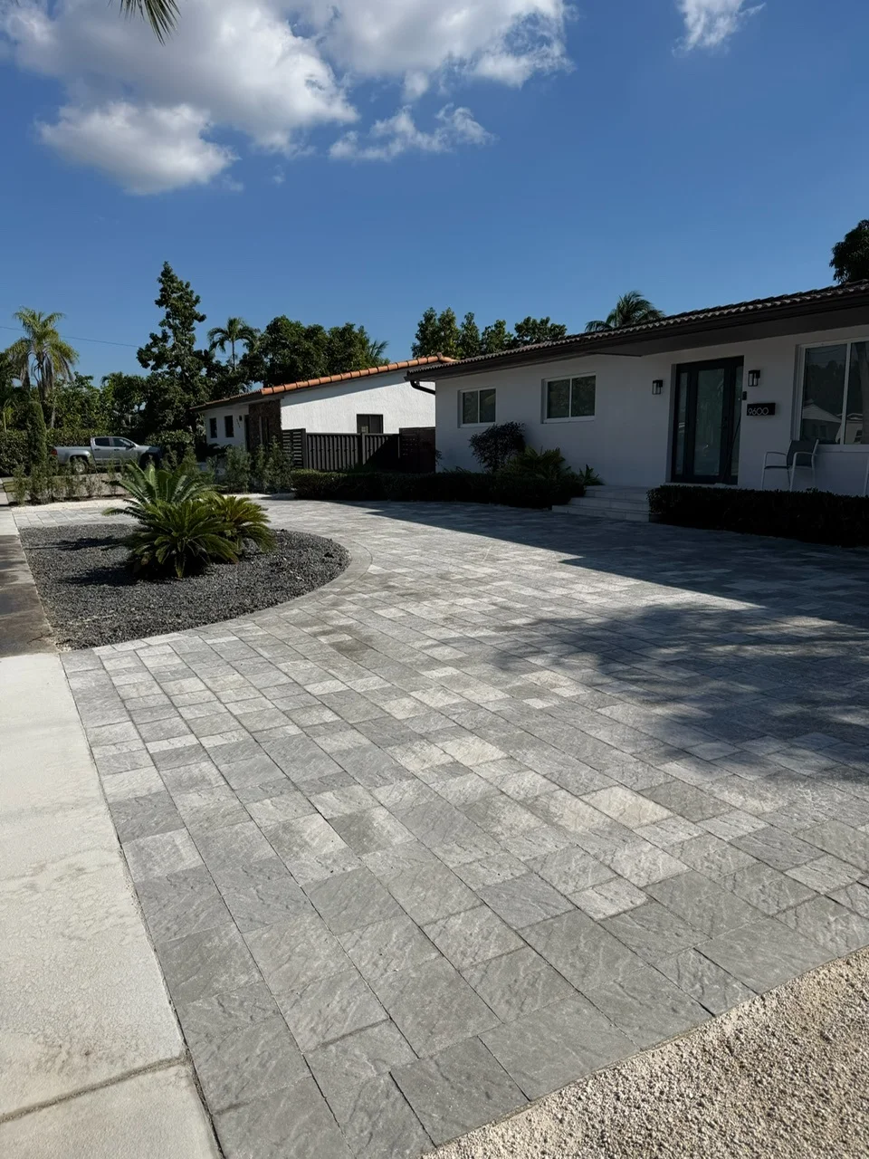 Grey stone-look pavers on a driveway wrapping a palm and river-rock island, Miami, FL