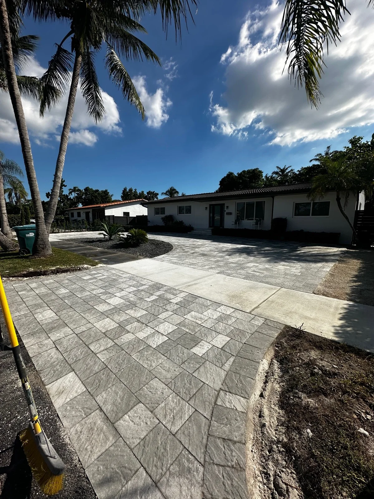 Grey stone-look paver driveway framed by palm trunks at a white house, Miami, FL