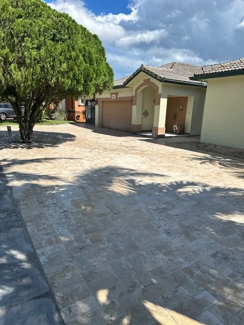 Travertine paver driveway curving past a tree to a home's entry arch, Miami, FL